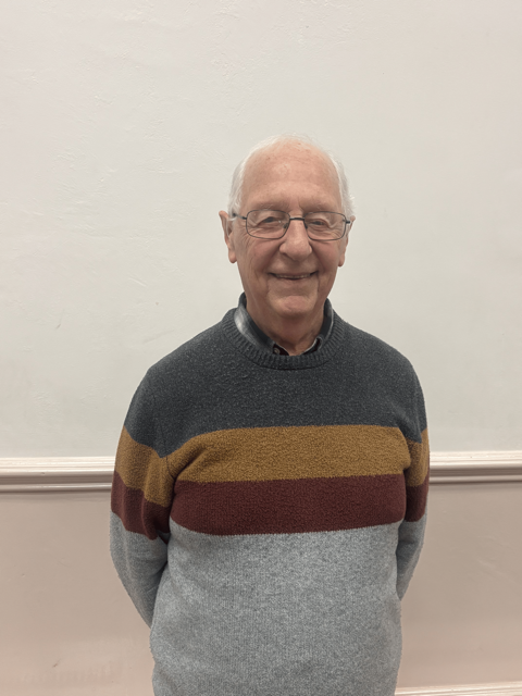 The image shows 85-year-old Eddie Allot smiling with his hands behind his back in a casual gesture